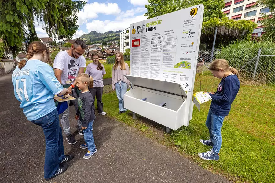 An der vierten Station steht das Fühlen und damit der Tastsinn im Mittelpunkt. Das Mädchen rechts knipst gerade ein Feld im Entdeckerweg-Flyer ab. Wer alle Stationen besucht und abgeknipst hat, darf am Ziel im Restaurant Acher ein Geschenk abholen.