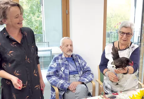 Giuseppa Conte jongliert ein Huhn auf ihrer Hand, derweil Karin Kälin und Leo Strüby dem Treiben mehr oder weniger begeistert zuschauen.